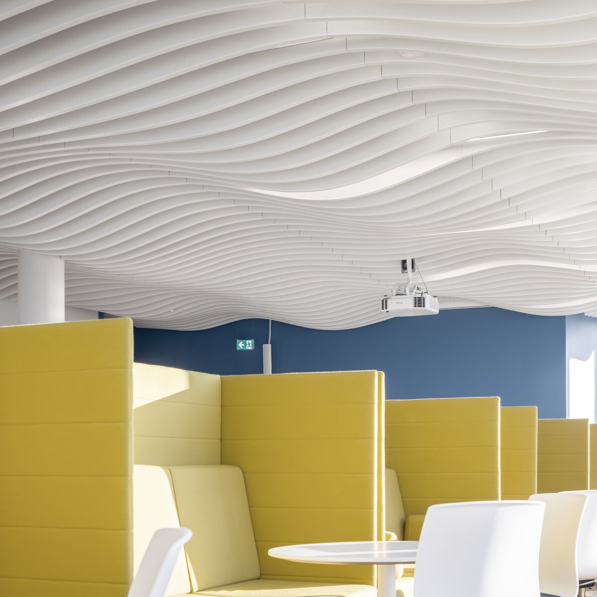 Moderne Kantine im Bürogebäude mit markanter Lamellendecke von Lindner und gelben Sitznischen für eine inspirierende Pausenatmosphäre.