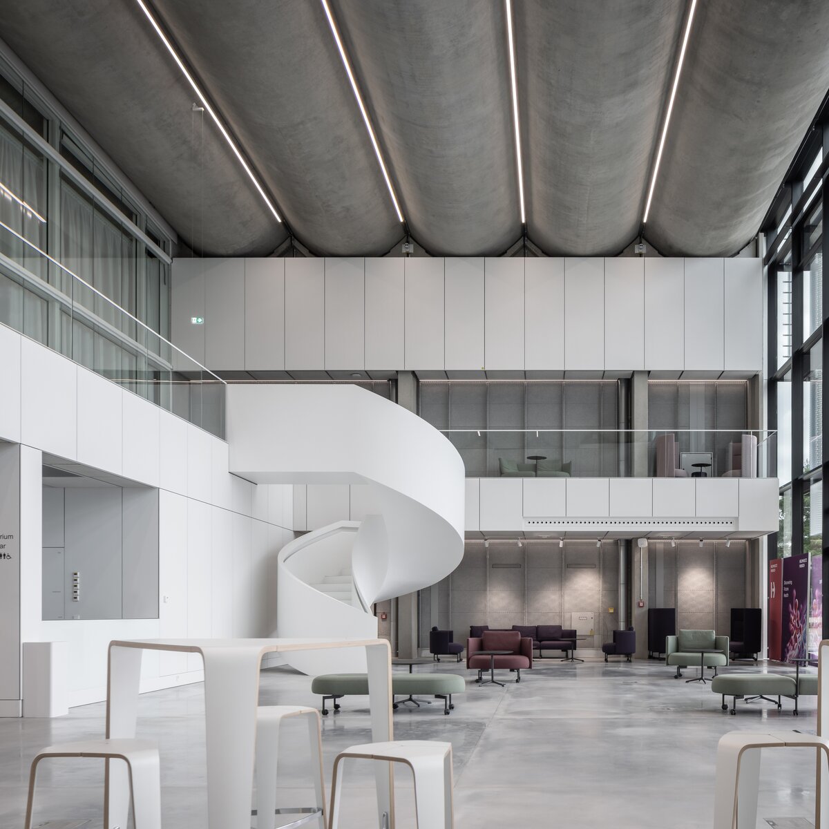 Modernisiertes Foyer des Helmholtz Zentrums München mit geschwungener Treppe, großflächiger Verglasung und modernen Sitzbereichen. | © © www.Lindner-Group.com