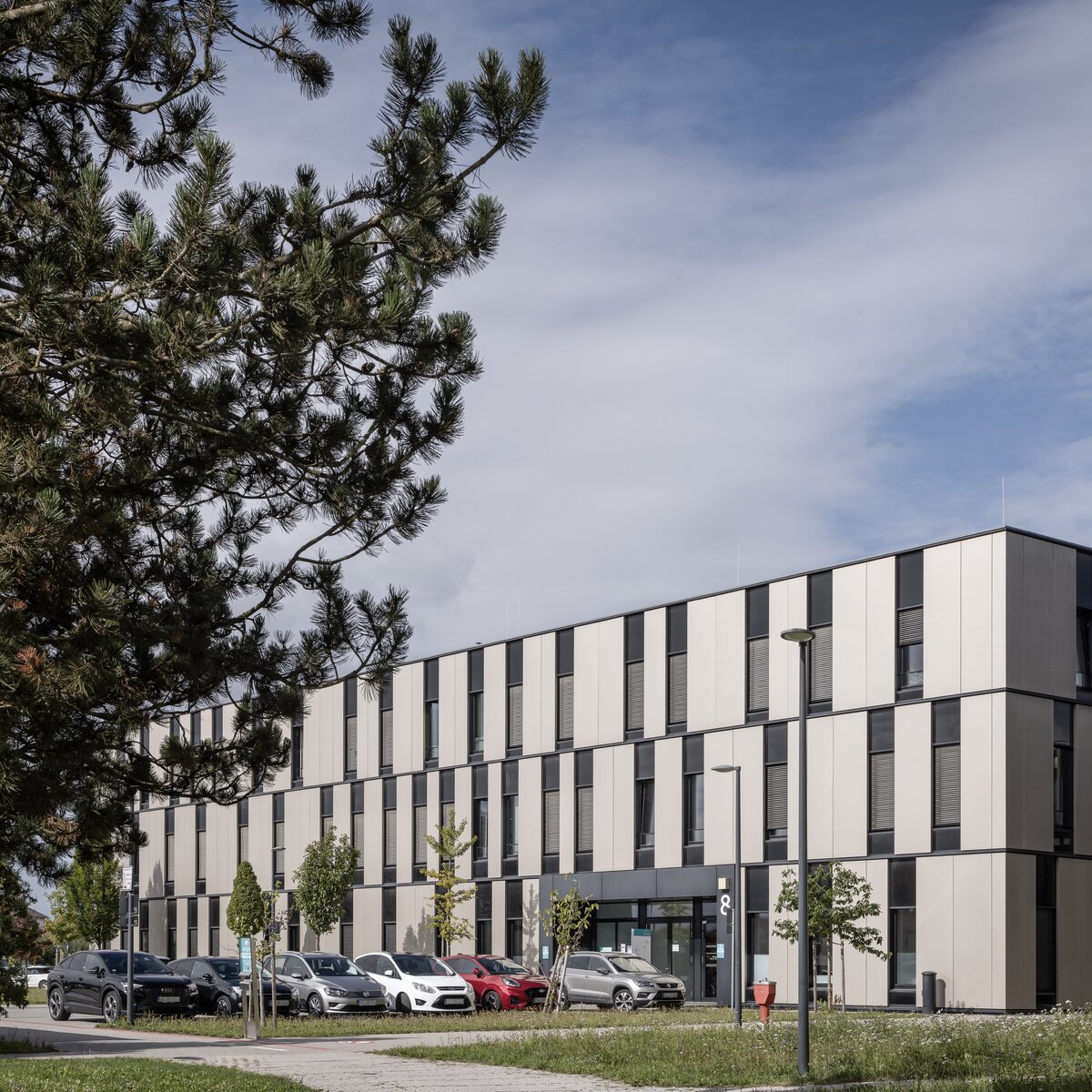 Außenansicht des InnKlinikums Altötting und Mühldorf in Altötting mit Parkplatz, Grünfläche und Bäumen; Lindner Group unterstützte den Umbau der Zentralapotheke mit eigenen Produkten. | © © www.Lindner-Group.com