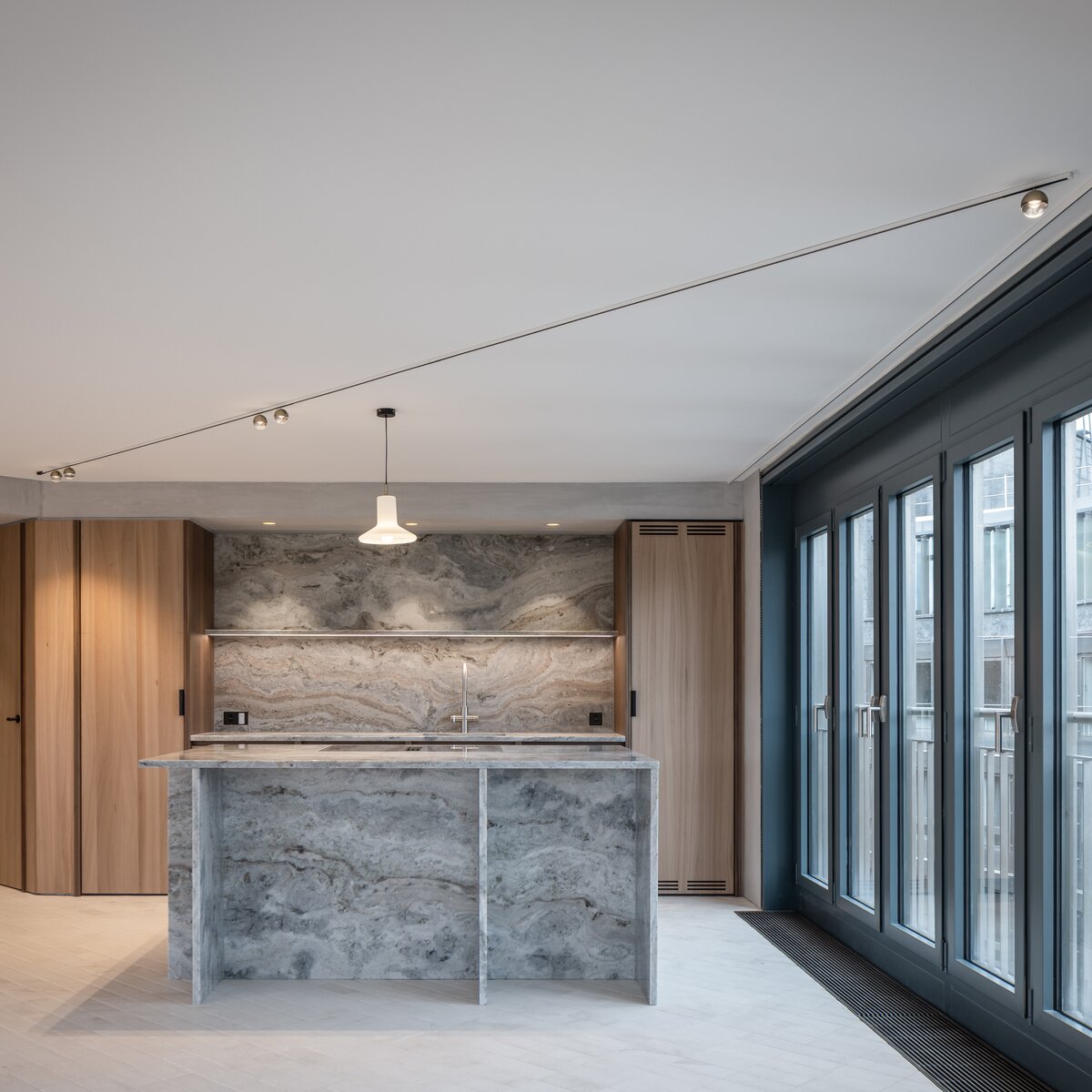 Moderner Küchenbereich mit heller Marmor-Kücheninsel, Fensterfront und hochwertiger Holzvertäfelung in stilvollem Innenraum | © © www.Lindner-Group.com