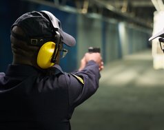 Ein Mann mit Kopfhörern schießt mit einer Pistole auf eine Türe. | © Adobe Stock